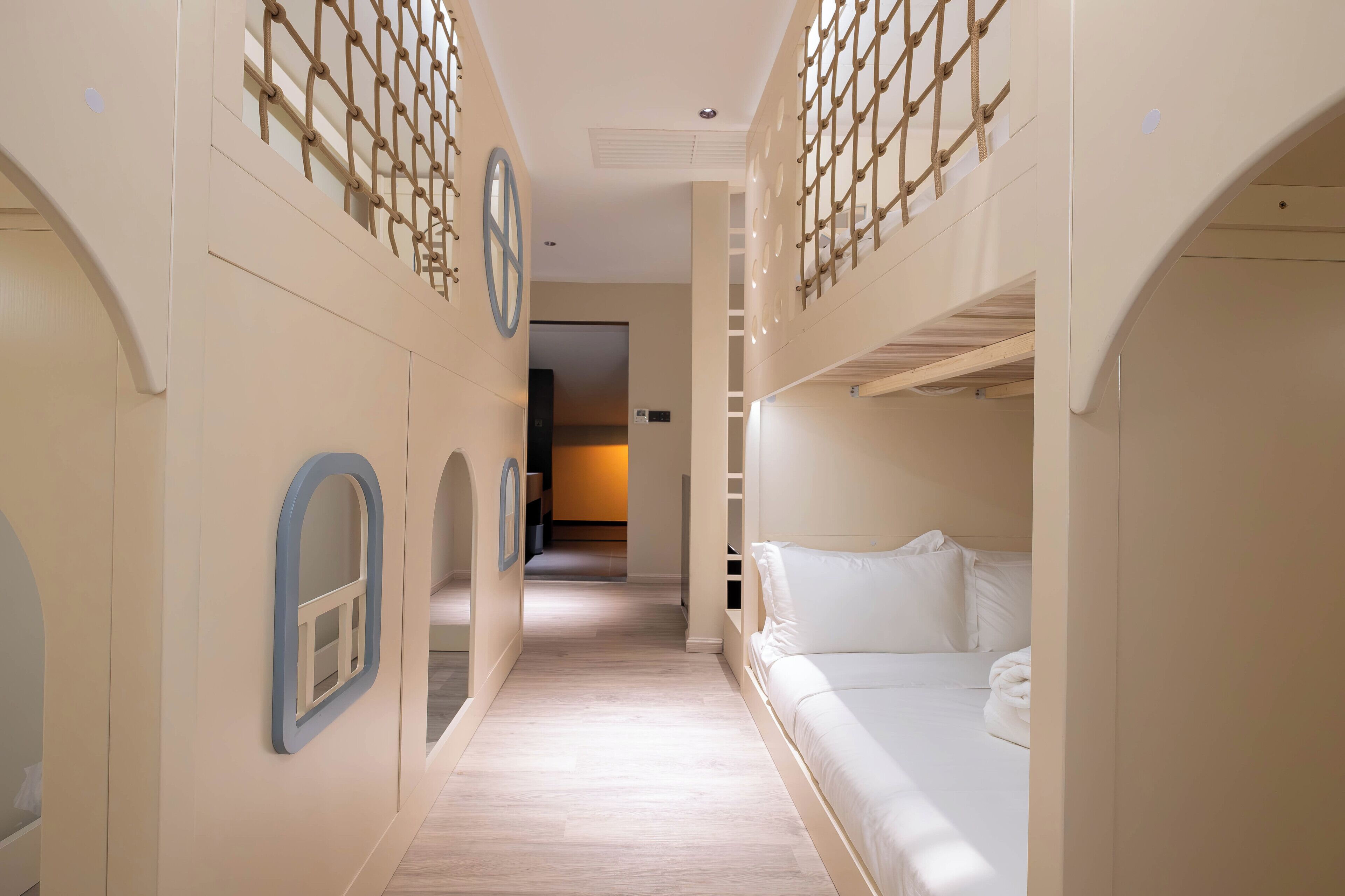Un pasillo de hotel con literas, piso de madera y una escalera que lleva a un nivel superior.