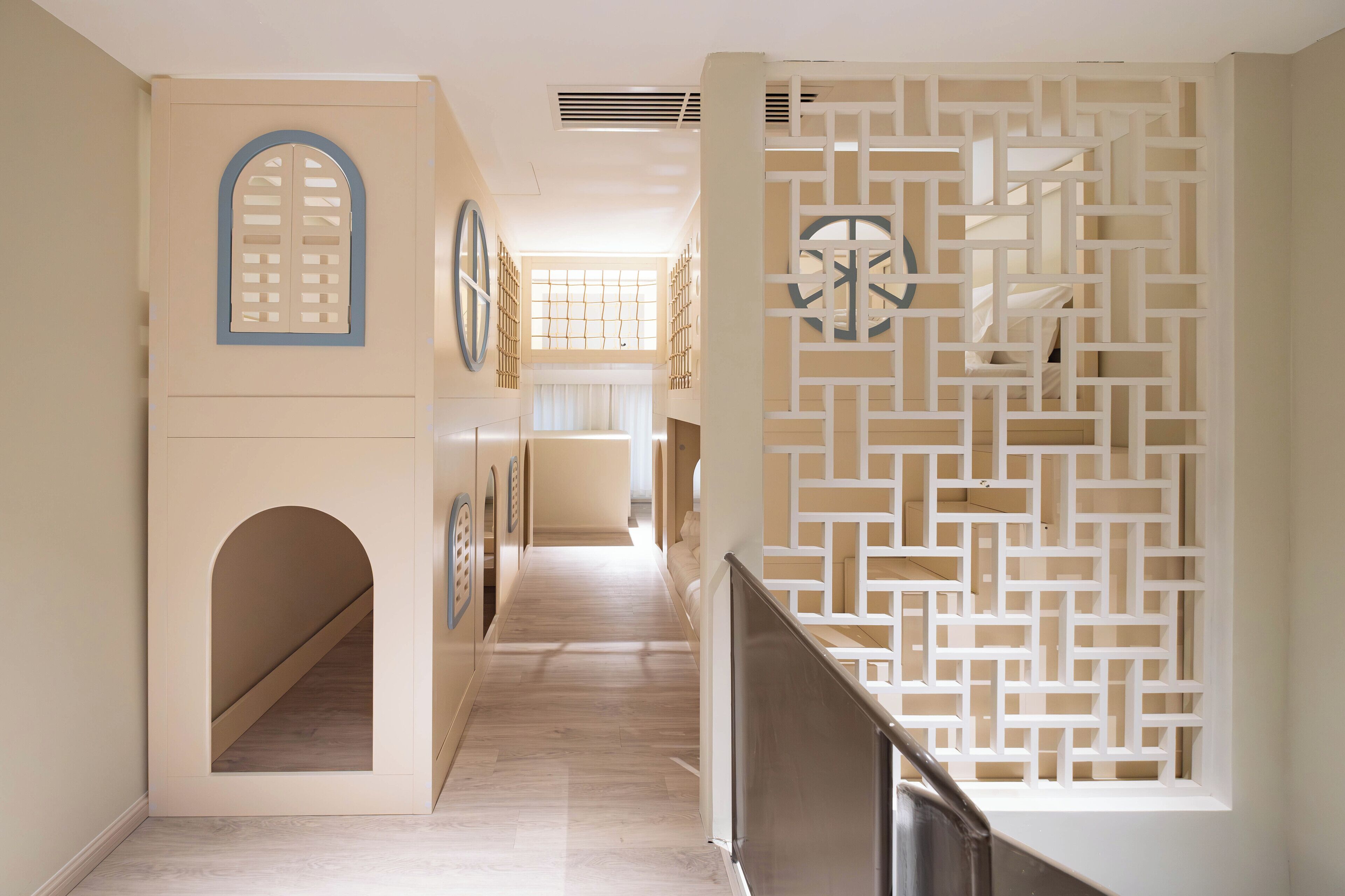 Un pasillo con piso de madera, un separador blanco decorativo con diseños geométricos y una escalera con barandilla de metal.