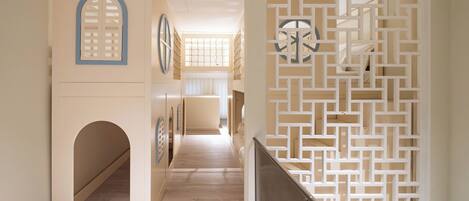 Un pasillo con piso de madera, un separador blanco decorativo con diseños geométricos y una escalera con barandilla de metal.