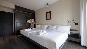 A neatly made bed with white linens and towels, a dark wooden wardrobe, a bedside table with a lamp, and a framed artwork on the wall.