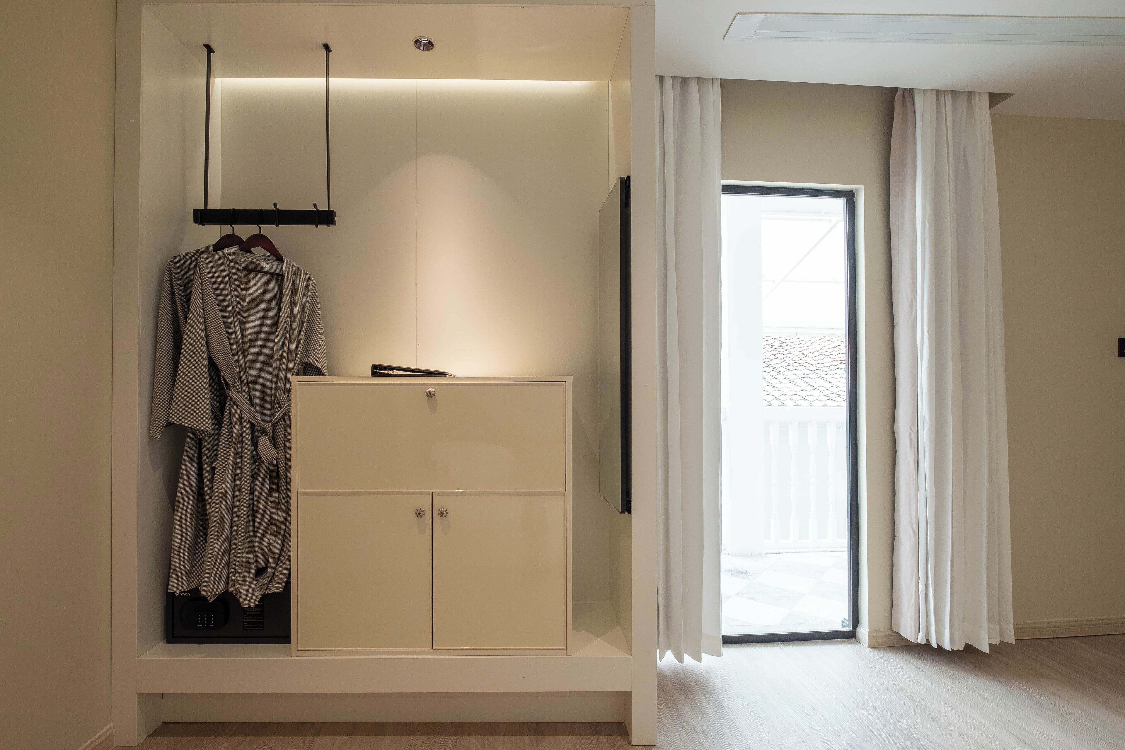 A modern bathroom with a built-in vanity, a robe hanging on a rack, and a sliding glass door leading to an outdoor area.