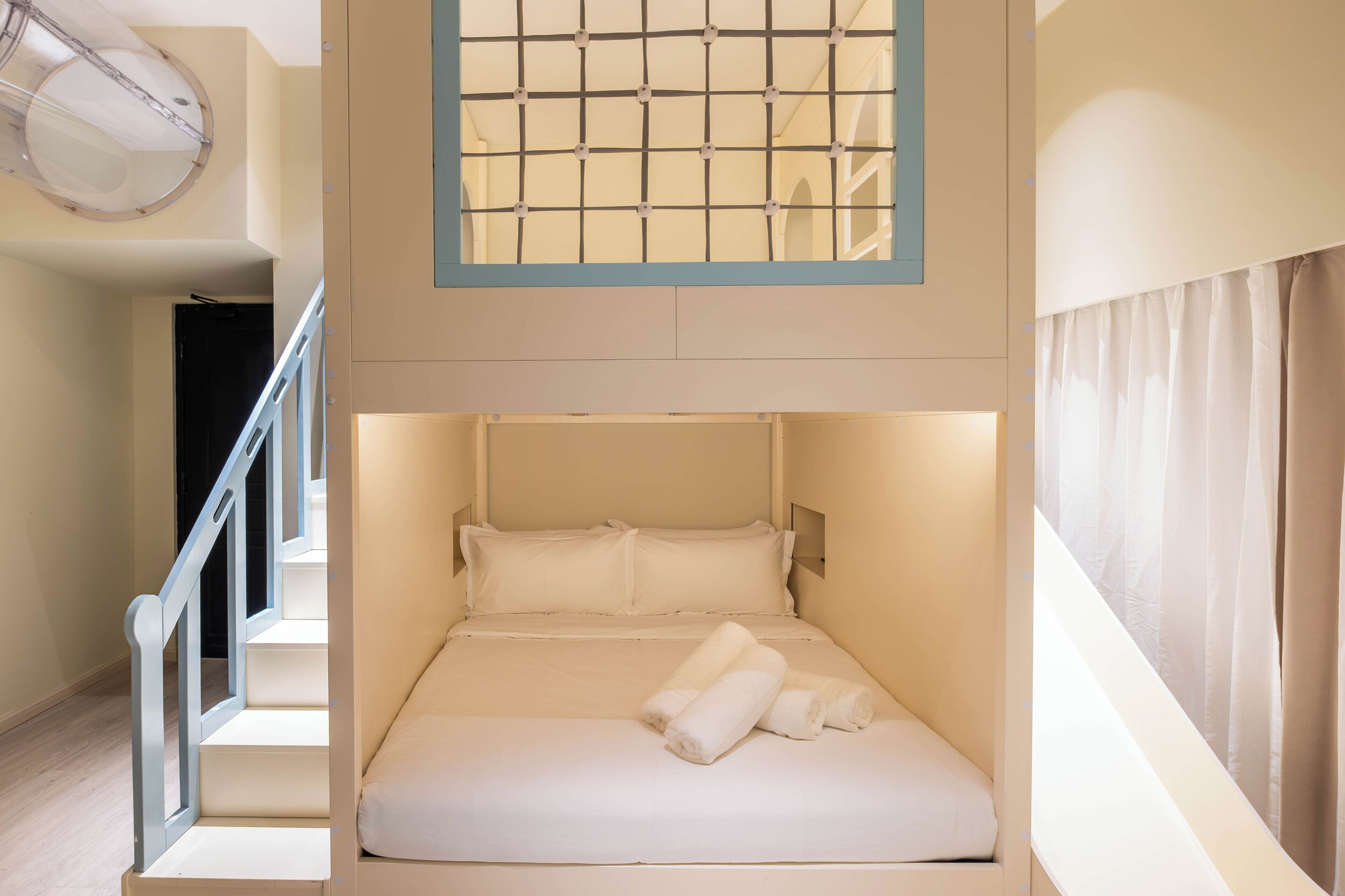 Un dormitorio moderno y compacto con literas, una pequeña ventana con diseño de cuadrícula y una escalera que lleva a otro nivel.