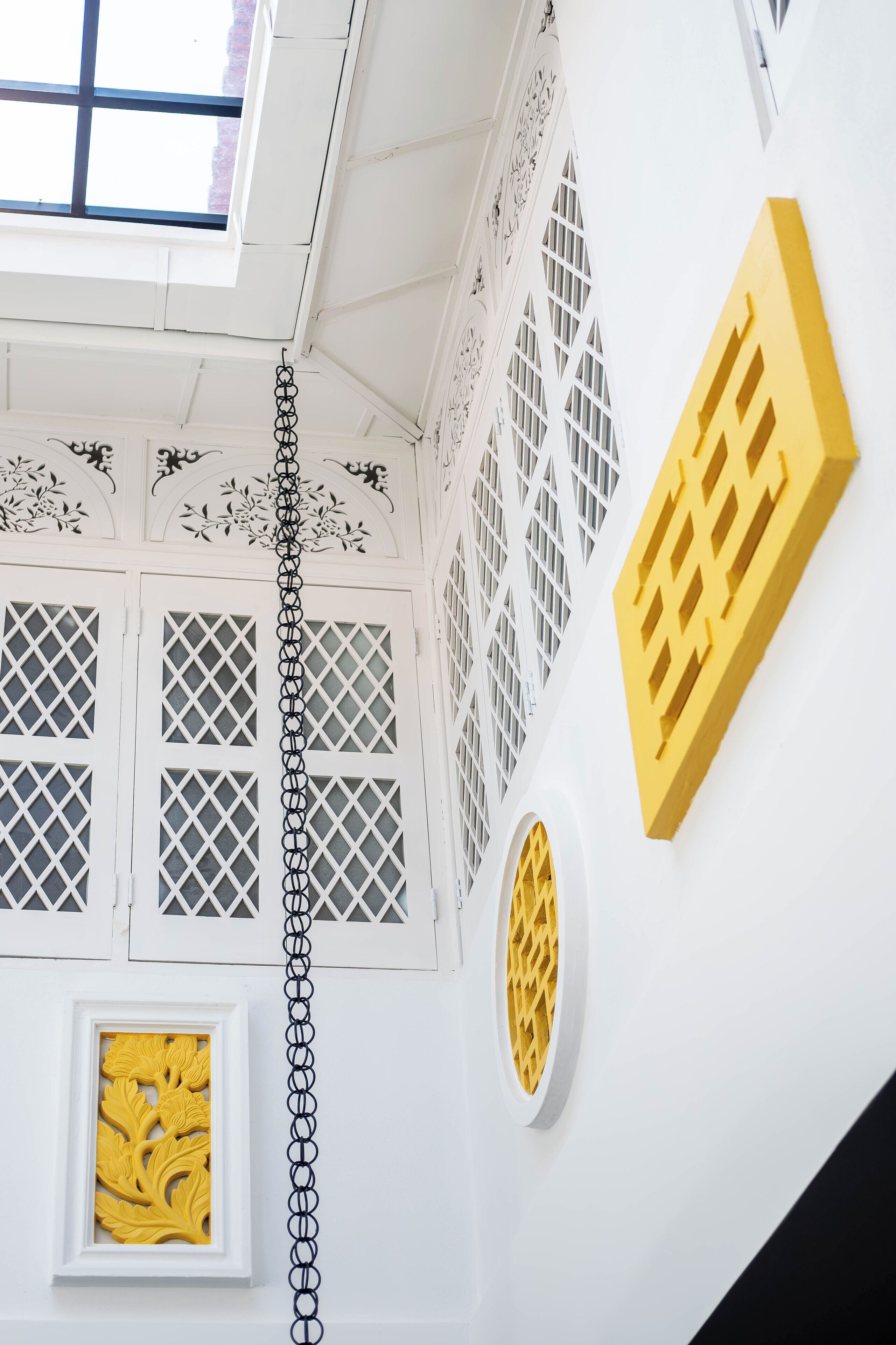 A room with a white ceiling, decorative lattice windows, a yellow wall feature, and a framed artwork.