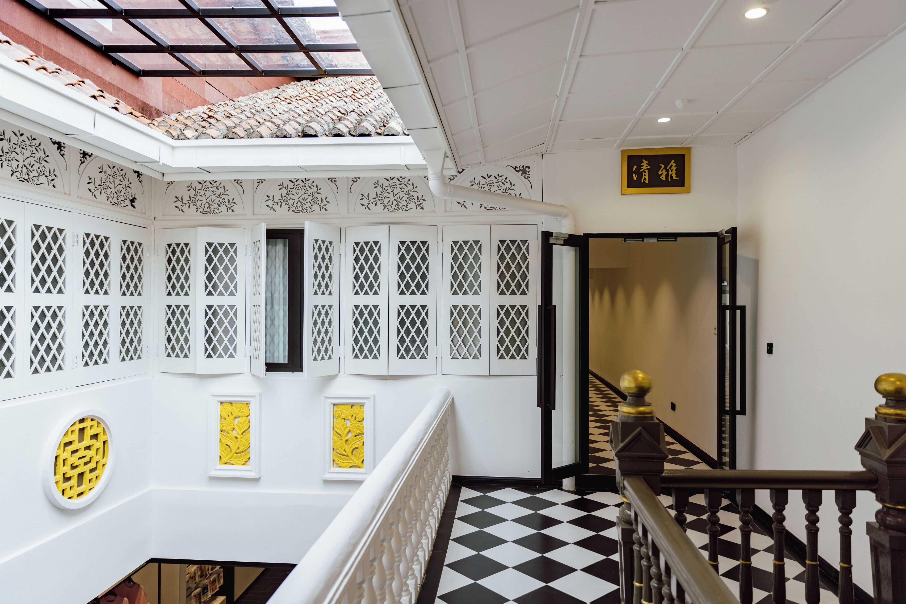 A hotel interior with a checkered floor, a staircase with a black and white railing, and a decorative ceiling with a skylight.
