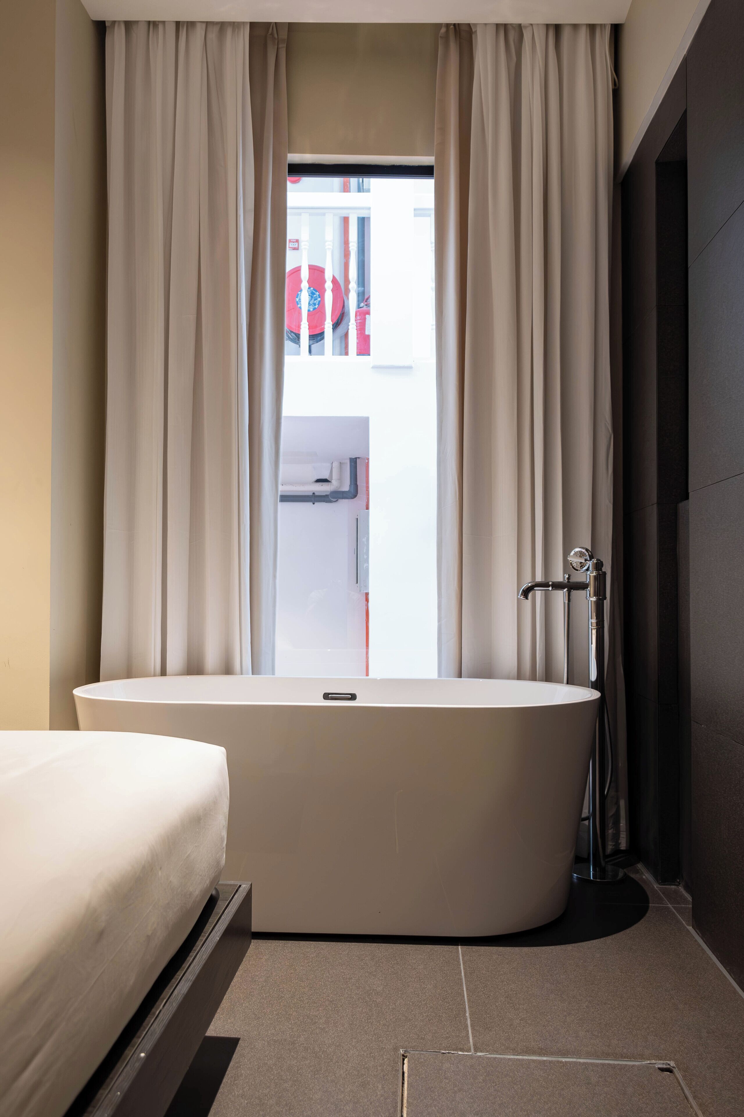 Ein modernes Badezimmer mit freistehender Badewanne, einer Duschkabine und Blick durch ein mit Vorhängen versehenes Fenster nach draußen.