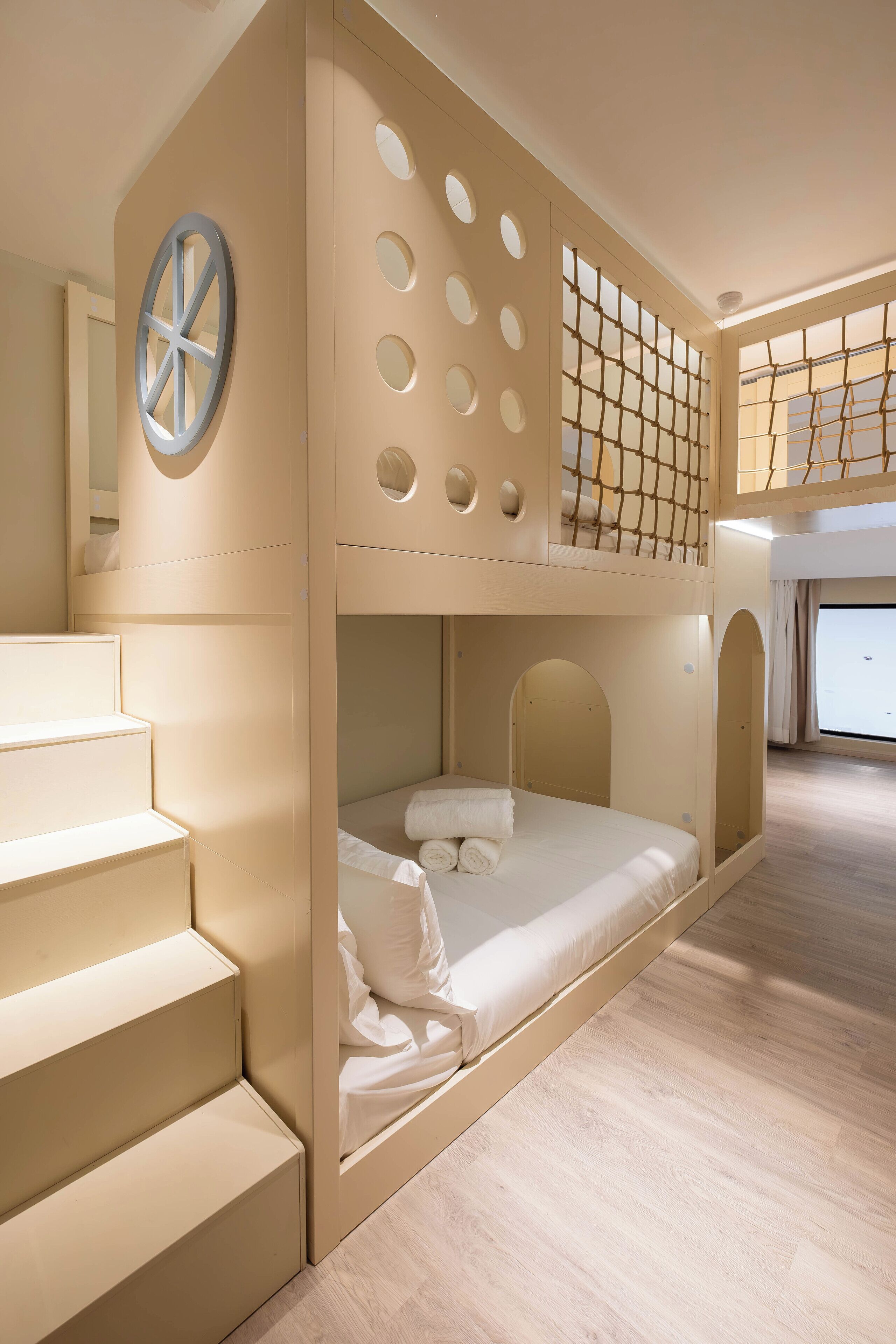 A bunk bed room with a circular window, a staircase, and a view of the outdoors.