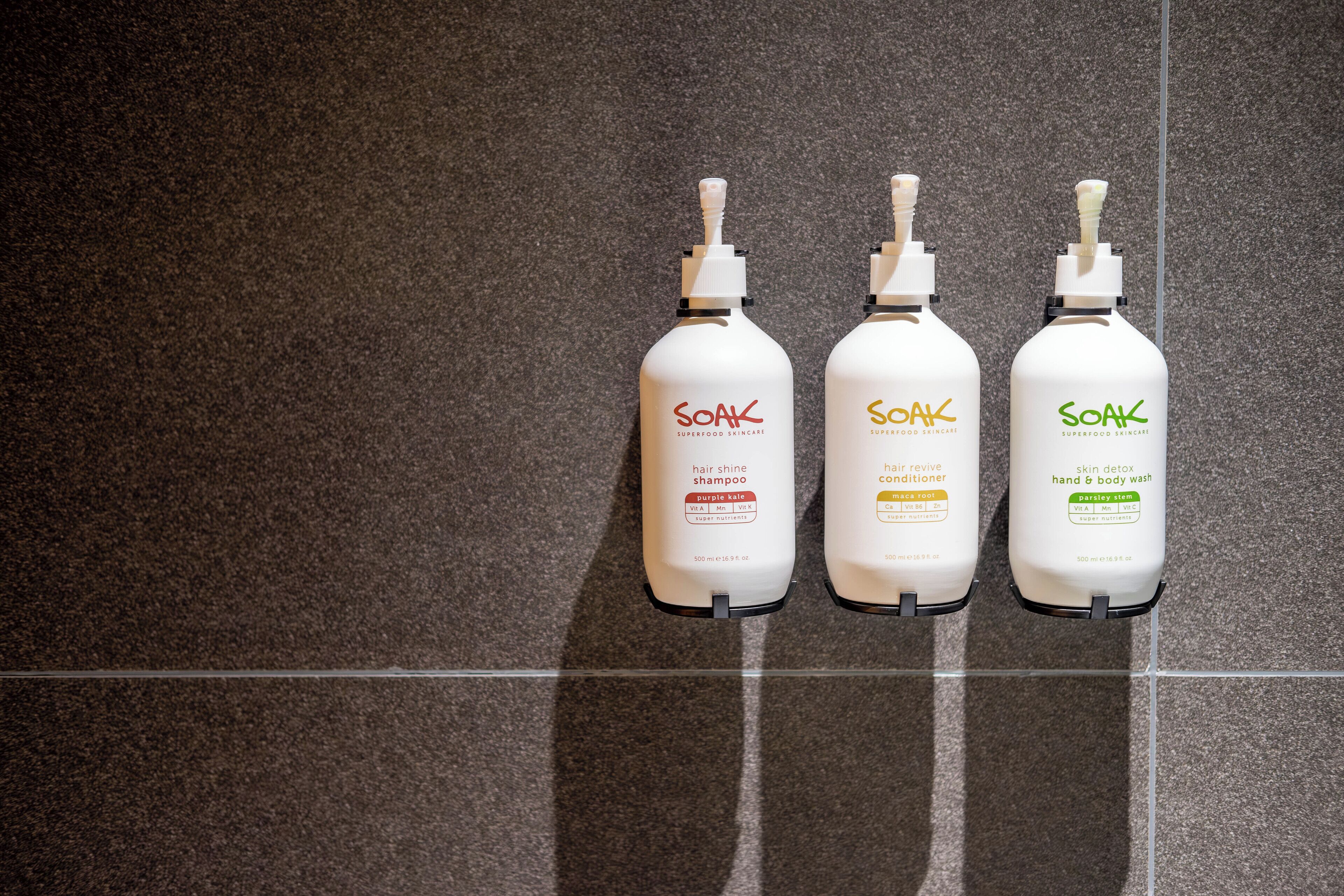 Three bottles of Soak hair care products on a tiled floor.
