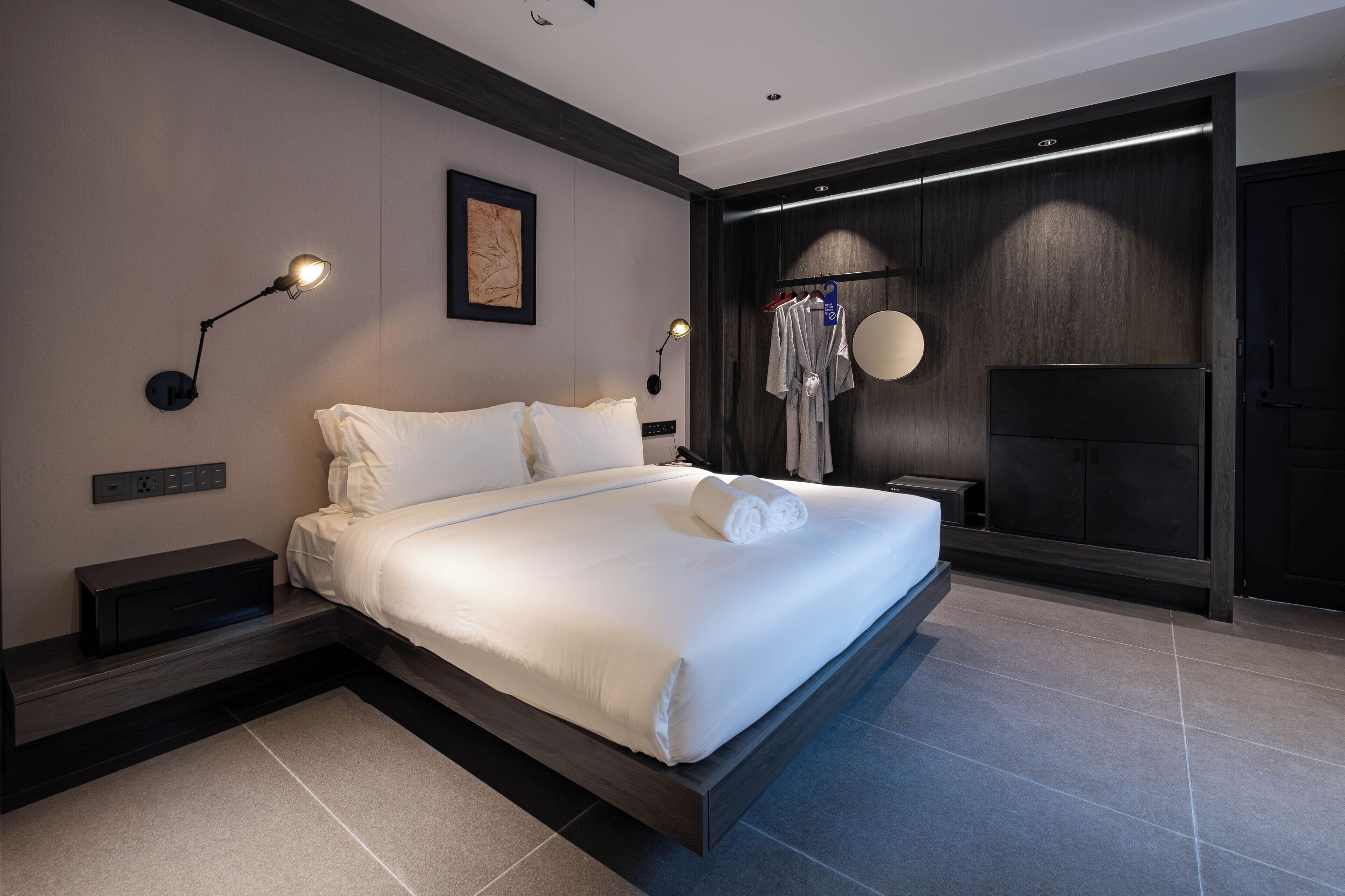 Ein modernes Hotelzimmer mit einem großen Bett, Nachttischen, einem an der Wand montierten Fernseher und einem Kleiderschrank.