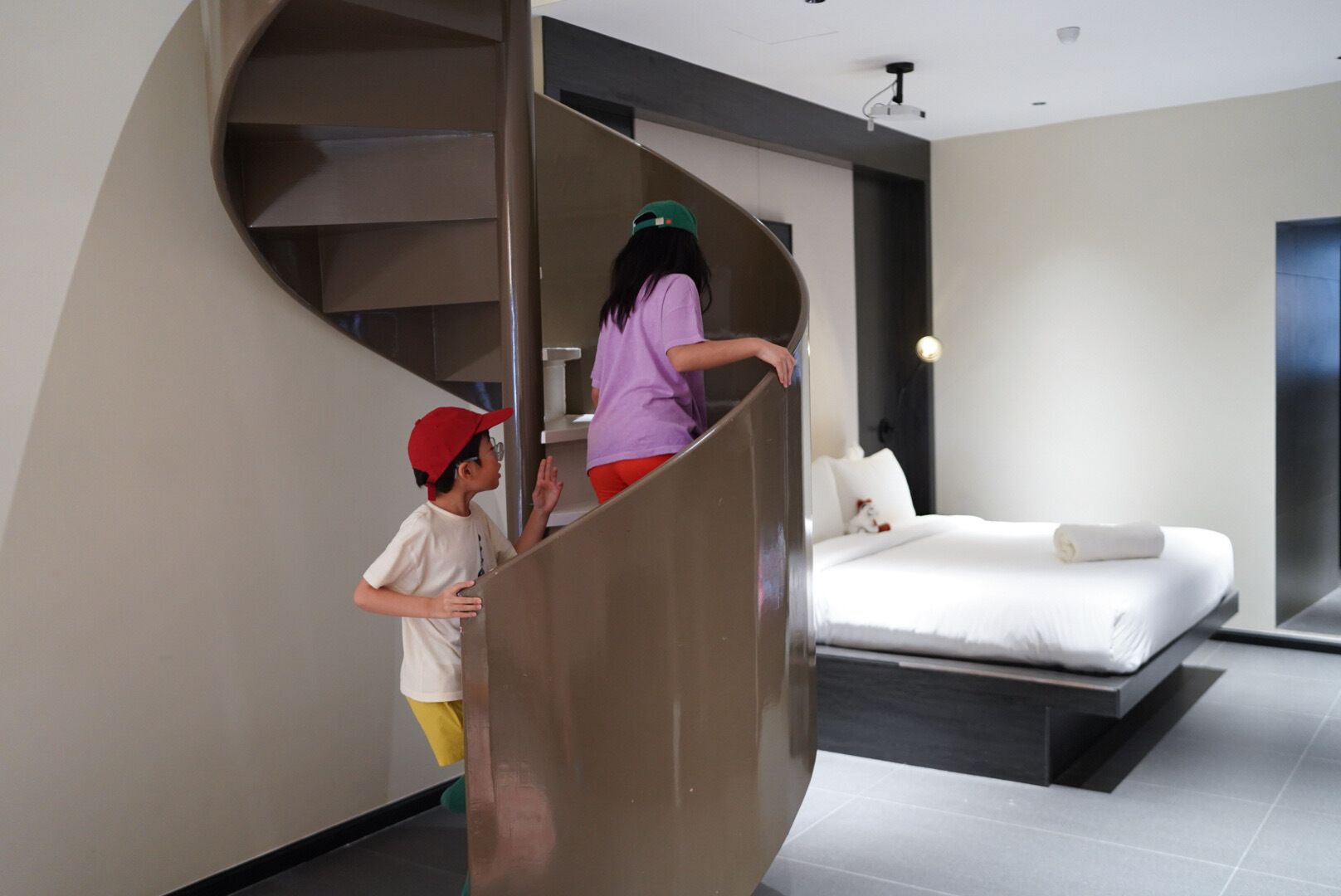 A modern bedroom with a curved staircase leading to a bed with white bedding and a pillow.