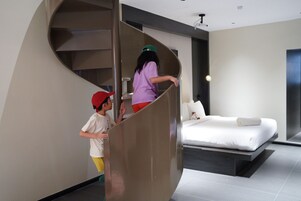 A modern bedroom with a curved staircase leading to a bed with white bedding and a pillow.