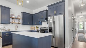 A modern kitchen with dark blue cabinets, a stainless steel refrigerator, and a central island. - Seaside Serenity Boutique Home (Gulfport)
