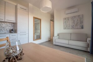 Eine moderne Küche mit weißen Schränken, einem Esstisch mit einer Glasvase voller Muscheln, einem weißen Sofa und einem großen abstrakten Gemälde an der Wand.