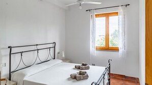 A bedroom with a bed, a ceiling fan, a window with curtains, and a nightstand with a lamp.