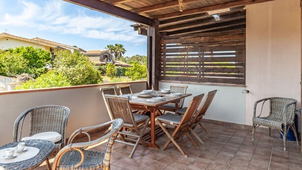 An outdoor patio with a wooden table and chairs, a view of houses and greenery, and a wooden ceiling.