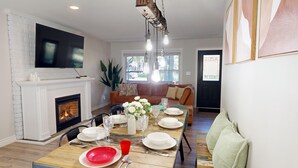 Un comedor con chimenea, un televisor montado encima y una mesa dispuesta para cuatro personas, con platos, vasos y cubiertos.