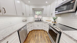 Cocina con armarios blancos, lavavajillas, microondas y ventana.