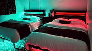 A bedroom with two beds, a window with blinds, a wall-mounted night sky poster, and three framed pictures.