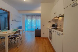 Une cuisine moderne avec des meubles blancs, un coin repas avec une table et des chaises, et une vue sur une pièce dotée d’une fenêtre et de rideaux.