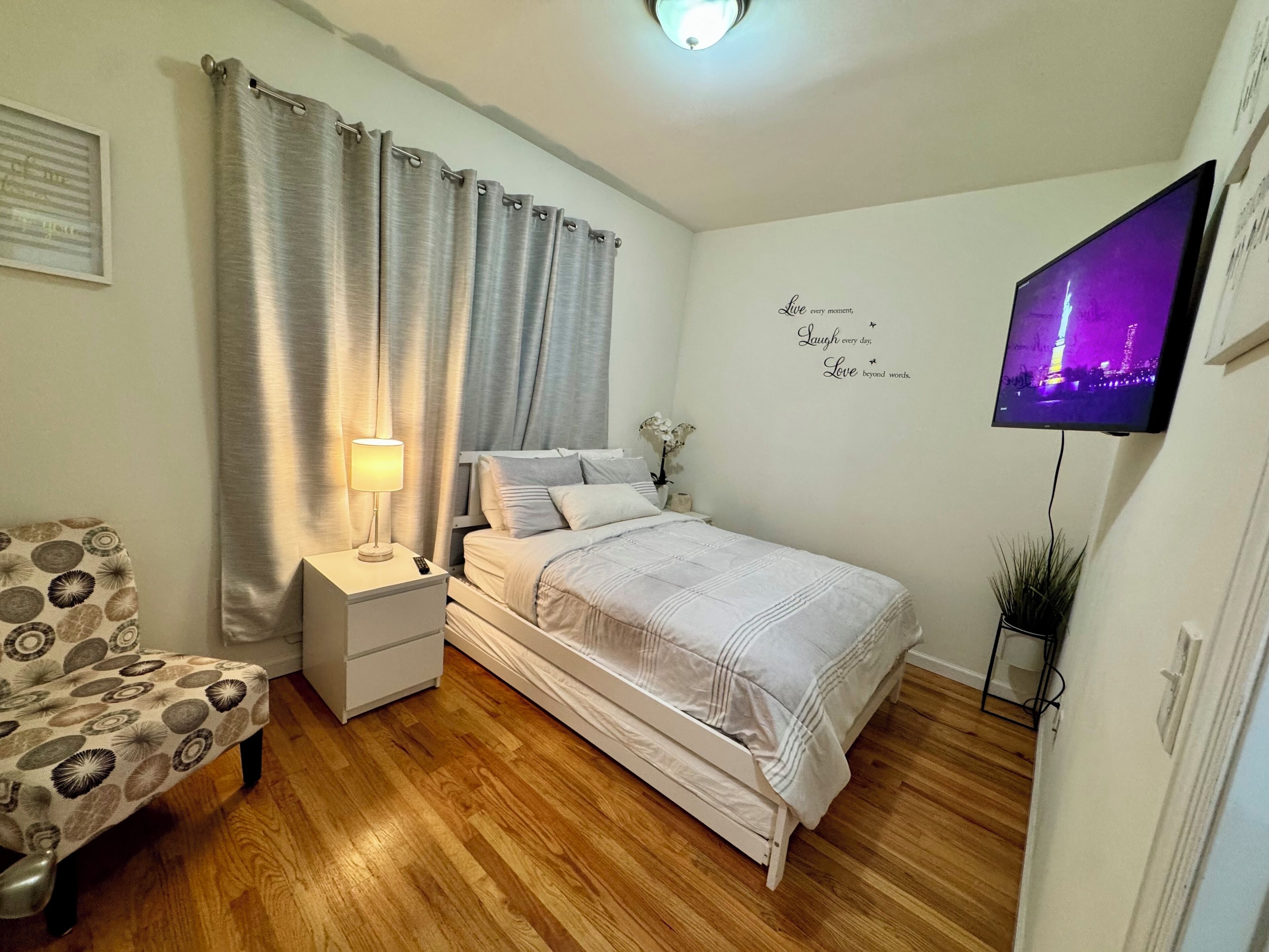 A bedroom with a bed, bedside table, lamp, chair, TV, and decorative wall art.