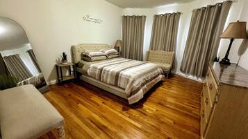 Une chambre à coucher bien rangée, avec un lit, une chaise, une table de chevet, une lampe et un miroir.