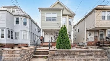 Una hilera de casas urbanas de dos pisos con una entrada central, un pequeño jardín delantero y una escalera de piedra que lleva a la puerta principal.