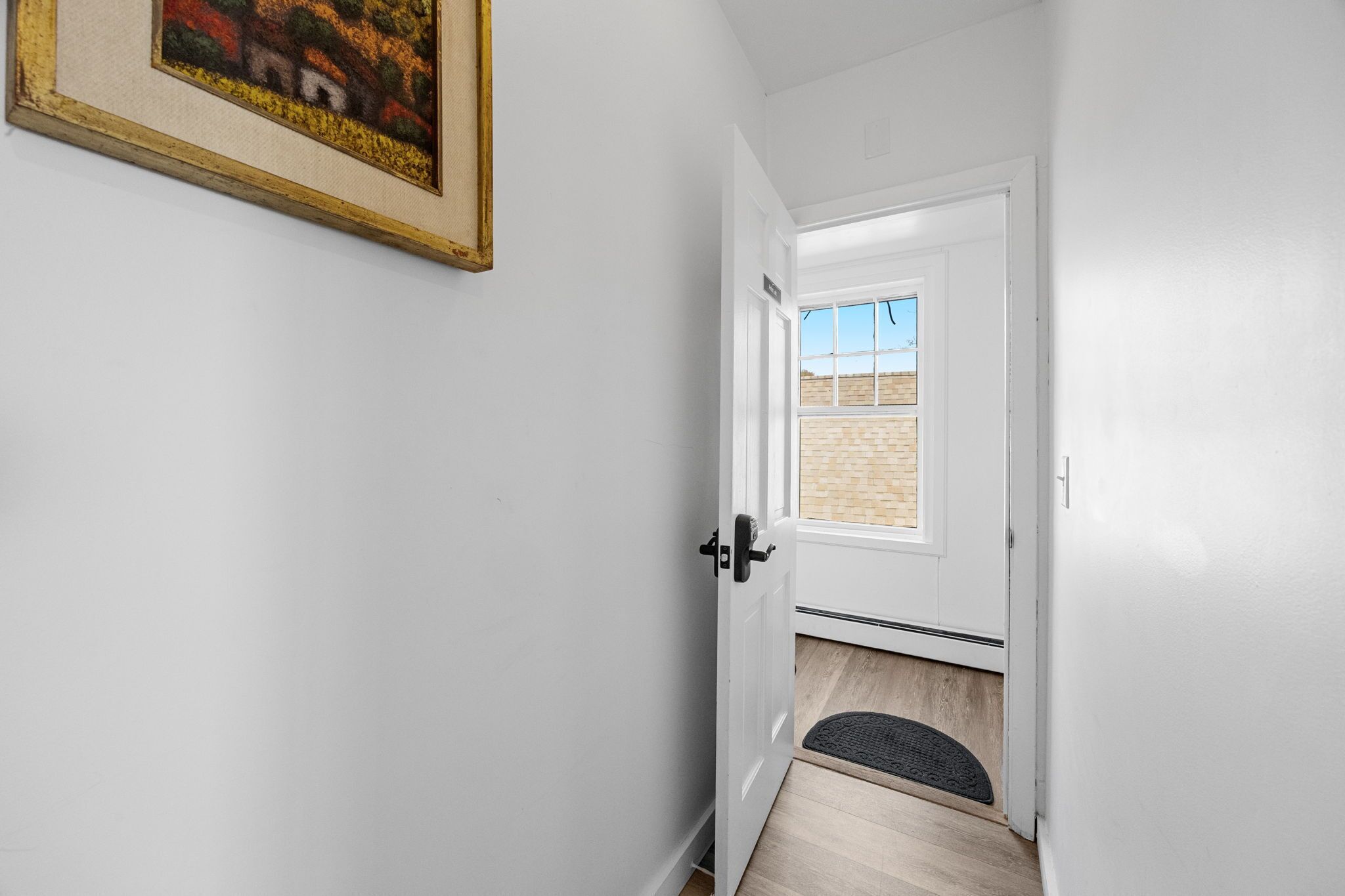 A hallway with a white door leading to a room with a view of a brick building.