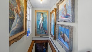 Un couloir aux murs ornés de tableaux classiques, doté d’un plancher en bois et éclairé par un lustre au plafond.