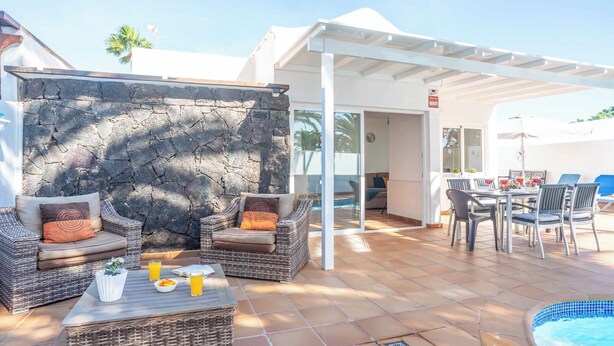 A patio area with wicker furniture, a stone wall, a pool, and a covered seating area. - Villa Canada (Tías)