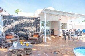 A patio area with wicker furniture, a stone wall, a pool, and a covered seating area. - Villa Canada (Tías)