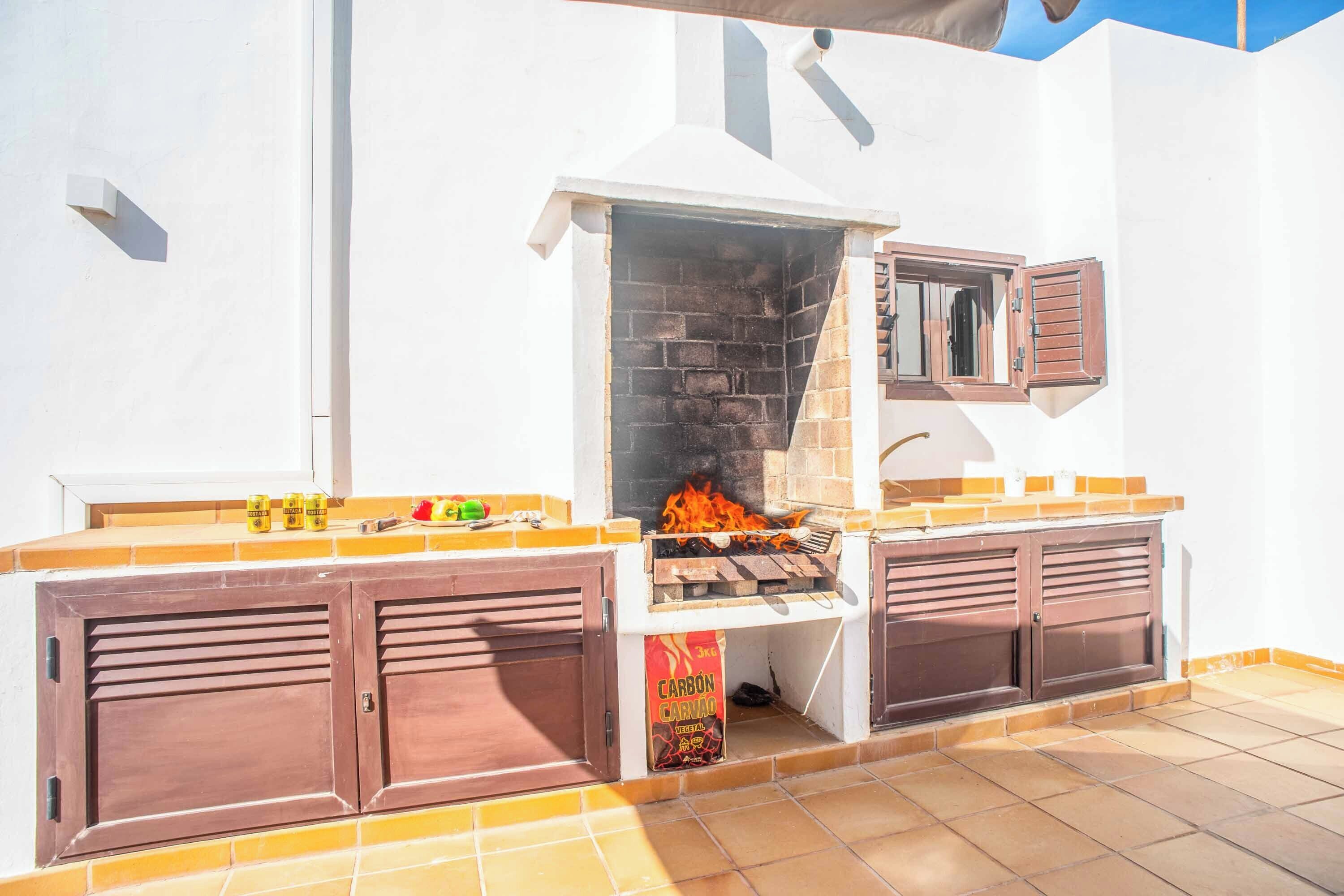 An outdoor barbecue area with a stone oven, wooden cabinets, and a bag of charcoal.