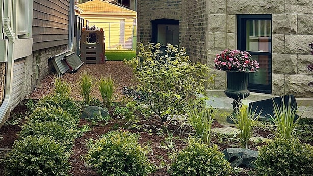 A courtyard with a garden, stone building, and wooden house.