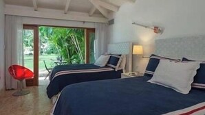 A hotel room with two beds, a red chair, and a view of greenery outside. - 4 Bedroom Golf Lake Front Villa in Casa de Campo (La Romana)