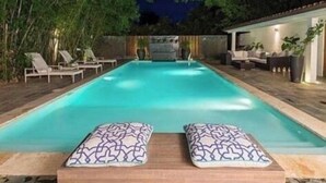 A swimming pool with lounge chairs and cushions, surrounded by a wooden deck and a covered seating area. - 4 Bedroom Golf Lake Front Villa in Casa de Campo (La Romana)