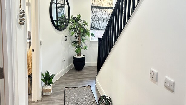 A modern hallway with a staircase, a potted plant, a mirror, and a patterned rug. - Stylish 2 Bed Apartment - Sleeps 4 - Free Parking (Dudley)