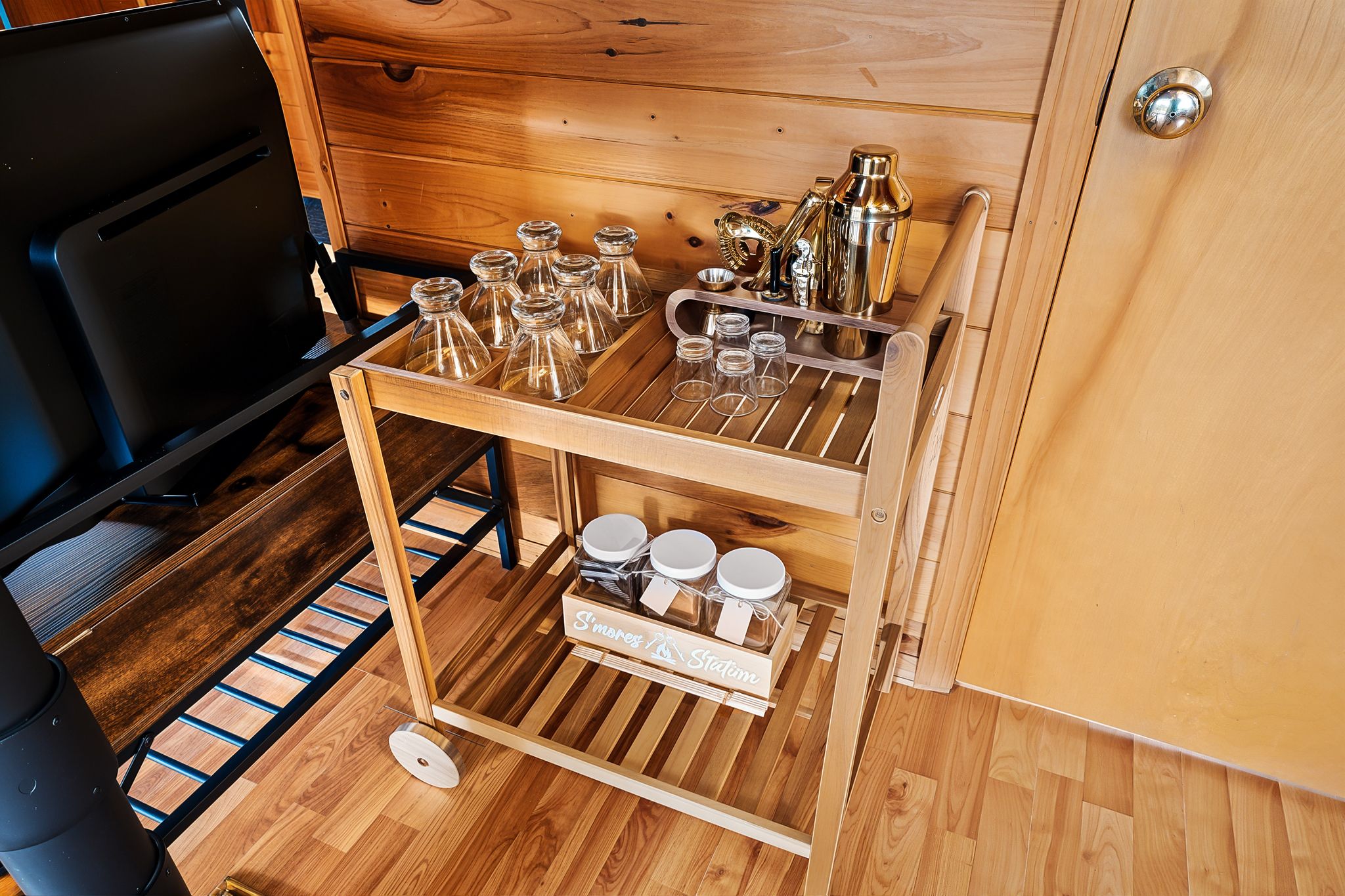 Un intérieur en bois avec un chariot à boissons contenant des verres, un shaker à cocktails et une bouteille.