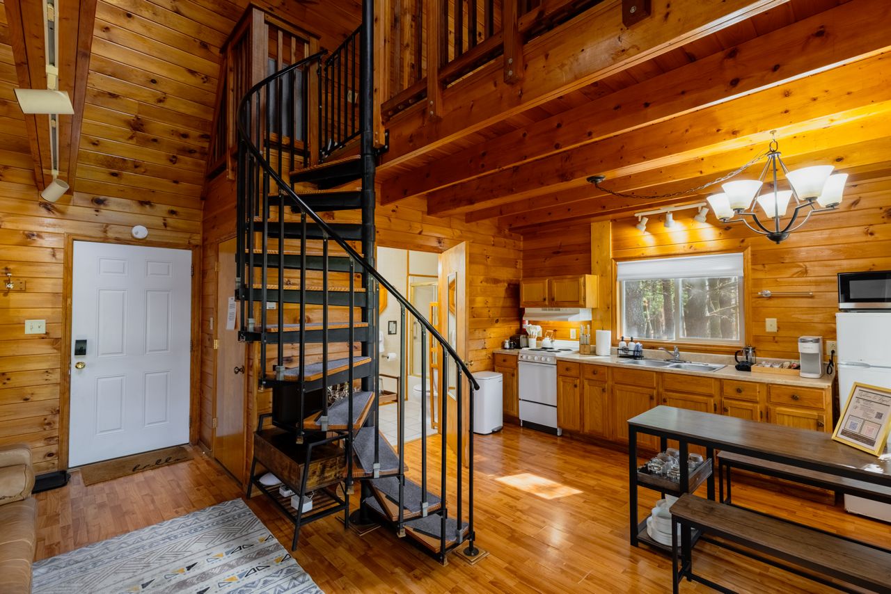 A wooden cabin interior with a spiral staircase, a kitchen with wooden cabinets, and a dining area.