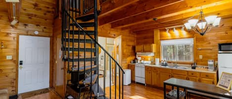 A wooden cabin interior with a spiral staircase, a kitchen with wooden cabinets, and a dining area.