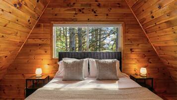 Une chambre à coucher dans une cabane en bois, avec un lit, deux lampes de chevet et une fenêtre donnant sur la forêt.