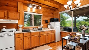Une cuisine rustique aménagée dans une cabane en bois, avec un poêle, un évier, un four à micro-ondes et un réfrigérateur.