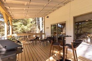 A covered outdoor deck with wooden flooring, chairs, a barbecue grill, and a table.