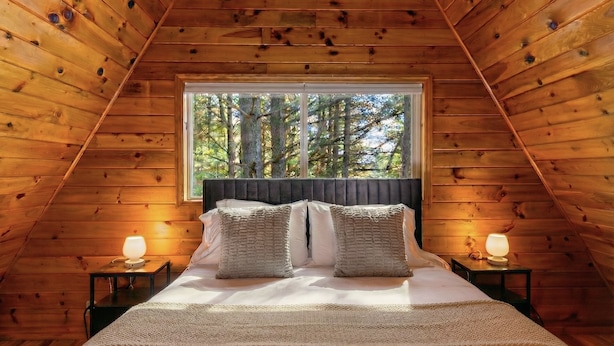Une chambre à coucher dans une cabane en bois, avec un lit, deux lampes de chevet et une fenêtre donnant sur la forêt.