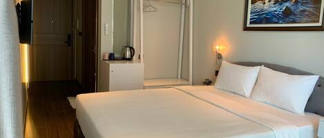 A hotel room with a bed, a nightstand, a wall-mounted TV, a painting, and a door leading to another room.