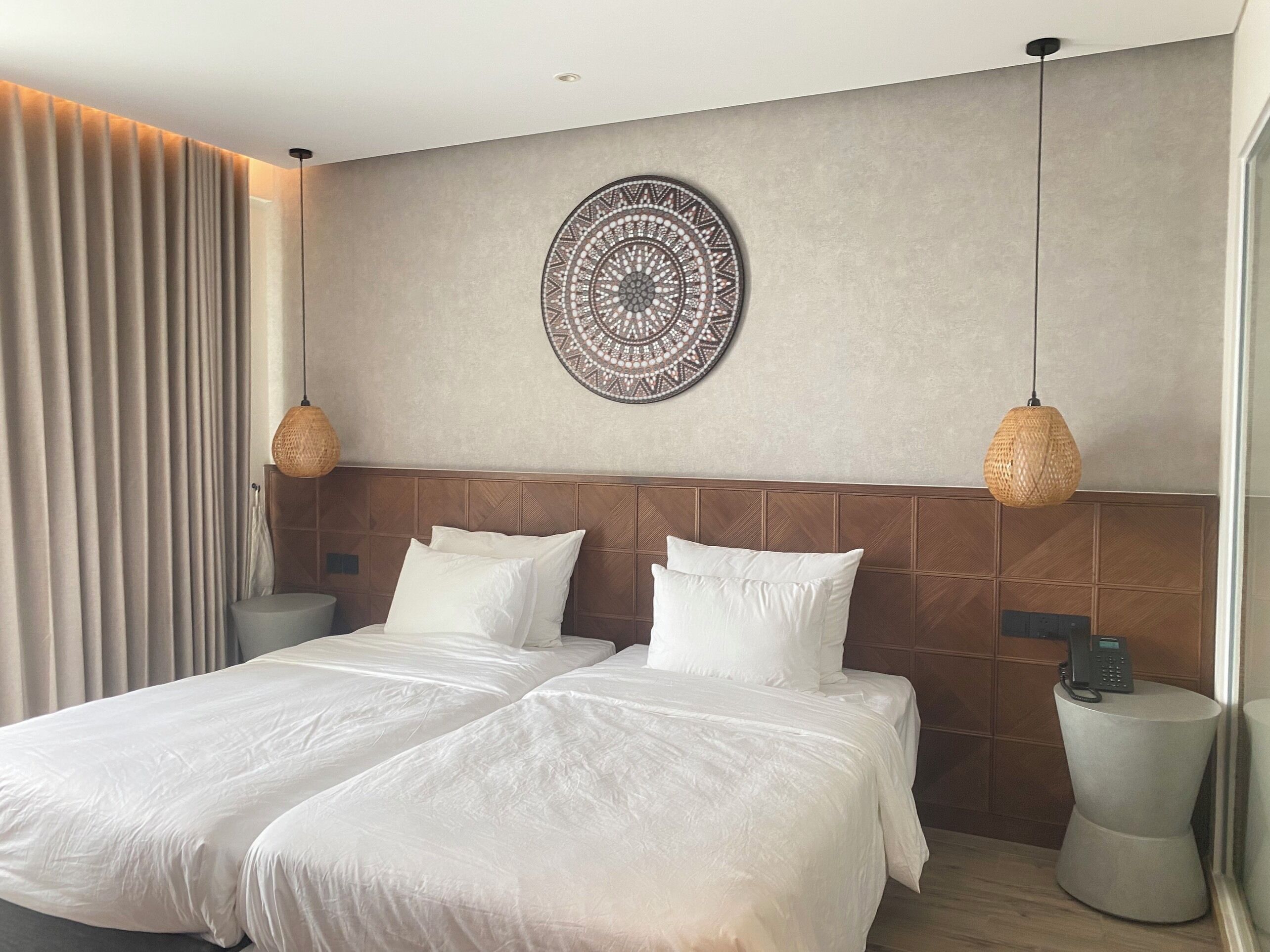 A modern hotel room with a large bed, two bedside tables, a wall-mounted phone, and a decorative circular wall piece.