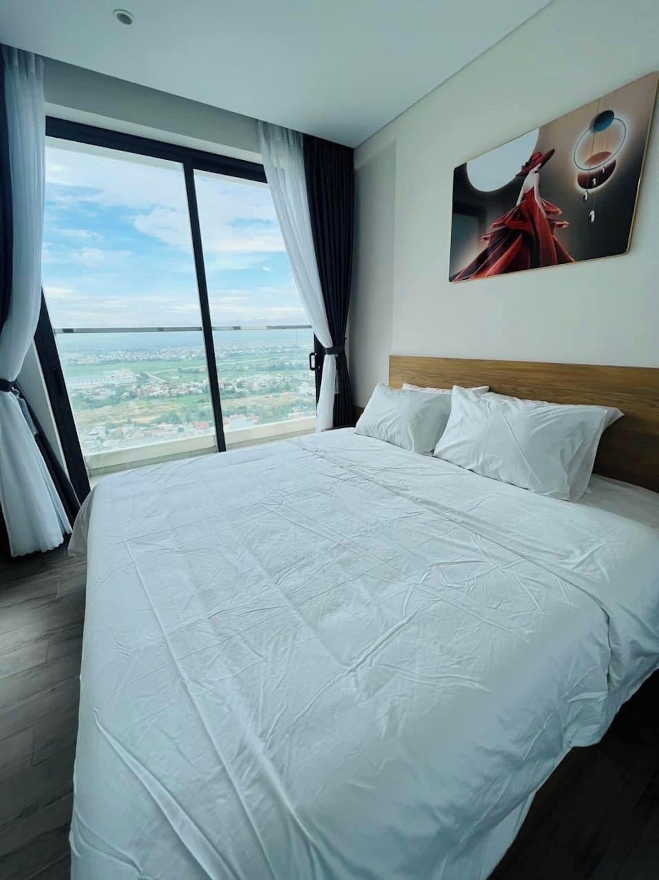 A hotel room with a large bed, a view of the city, and a painting on the wall.