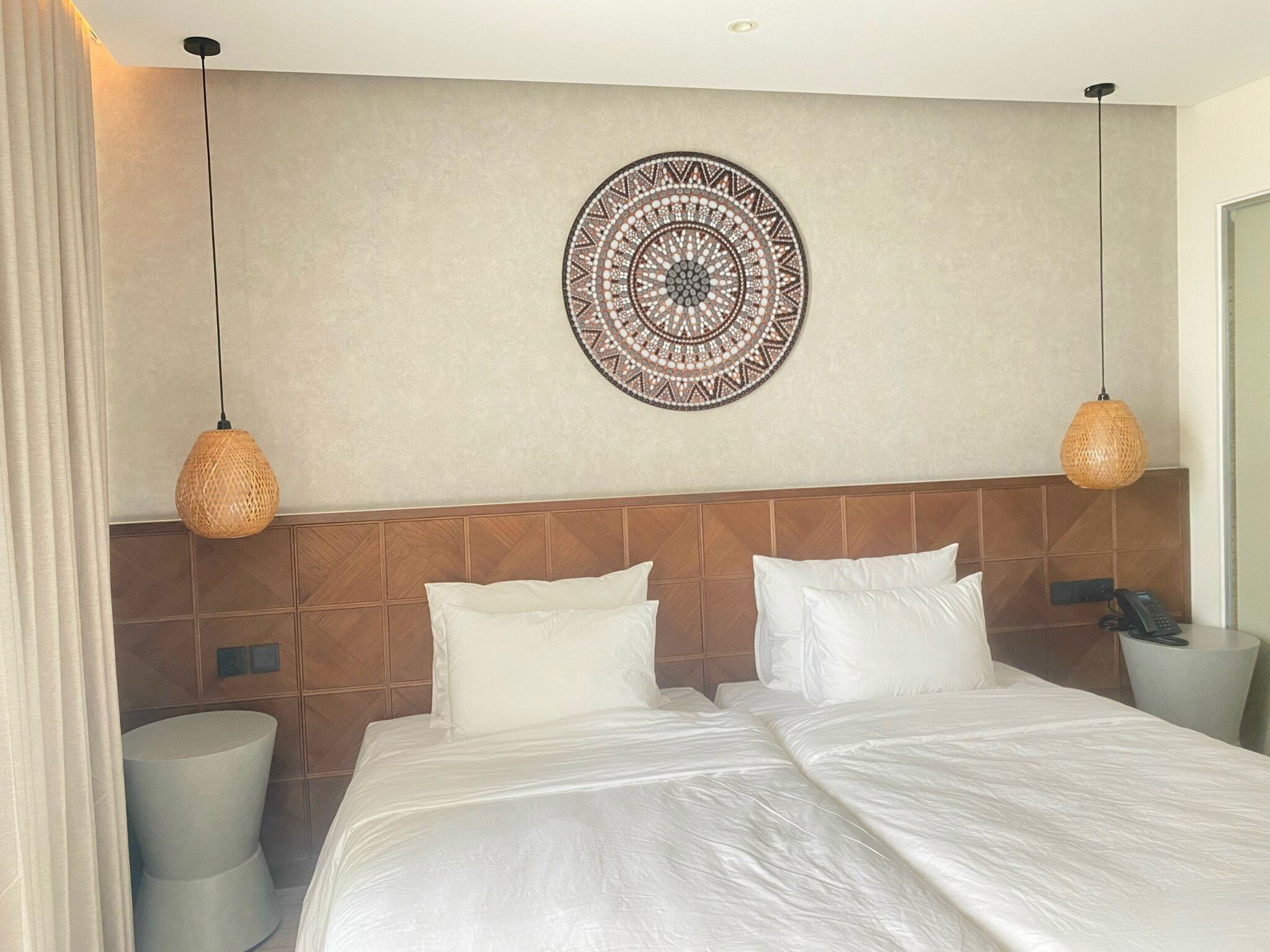A hotel room with a large bed, two bedside tables, a wall-mounted decorative item, and two hanging lamps.