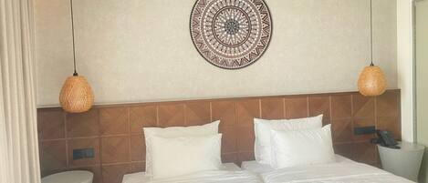 A hotel room with a large bed, two bedside tables, a wall-mounted decorative item, and two hanging lamps.