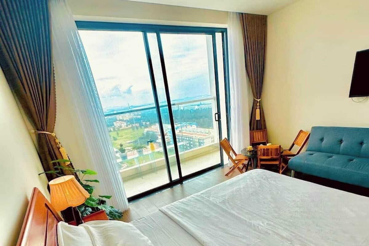 Habitación de hotel con una cama grande, un sofá, una mesita y vistas a la ciudad a través de la ventana.
