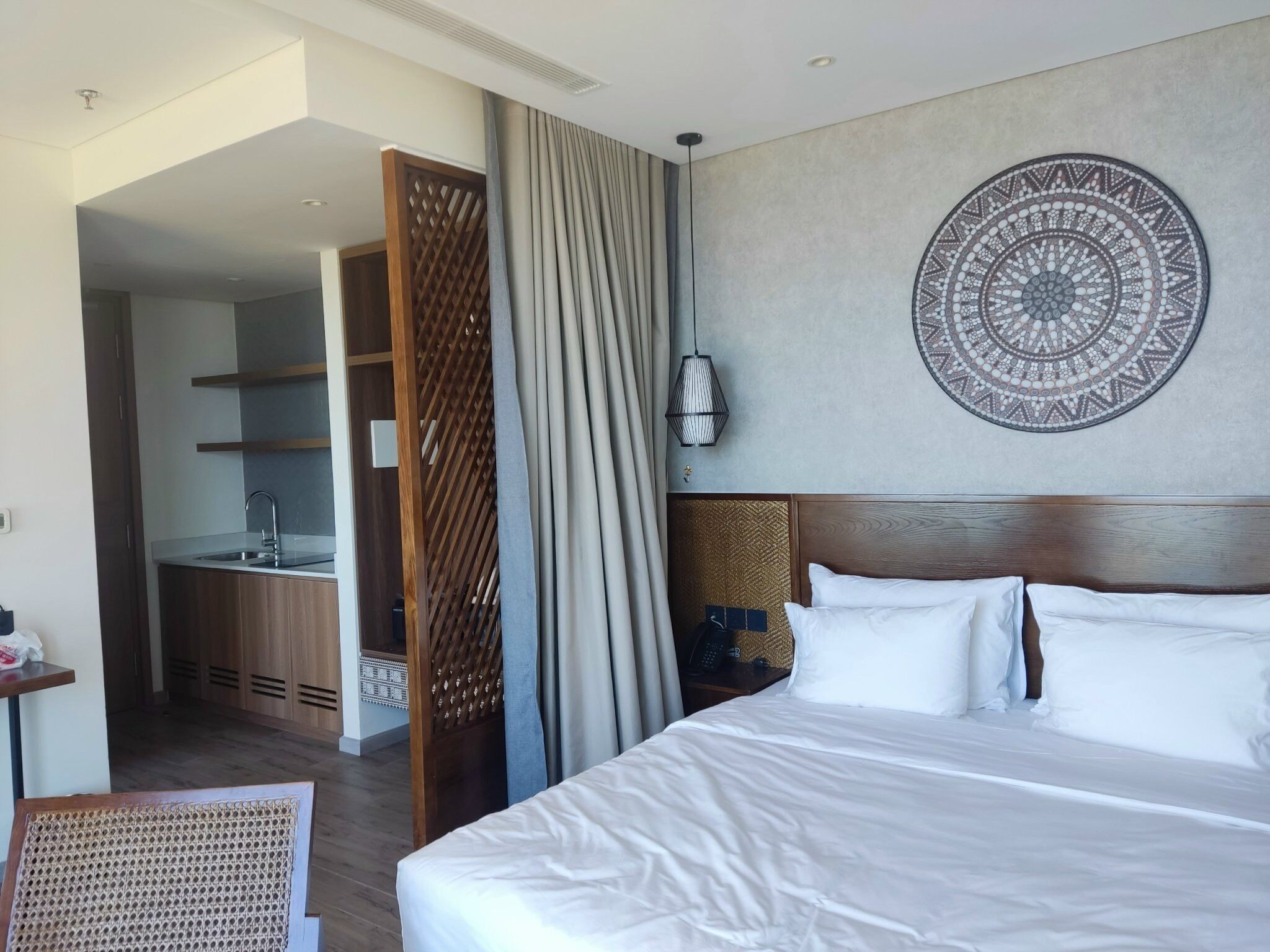 Habitación de hotel con una cama grande, un adorno circular en la pared, cabecera de madera y vistas al área de la cocina.