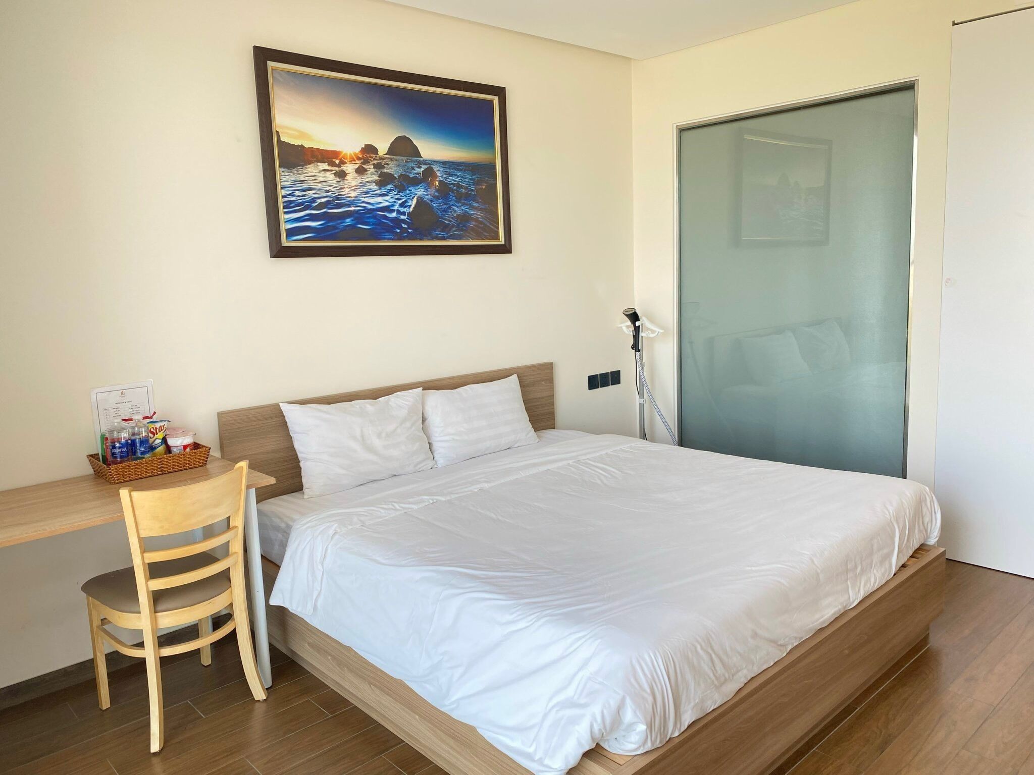 Ein Hotelzimmer mit einem Bett, einem Schreibtisch mit Stuhl, einem Bild an der Wand und einer Tür.
