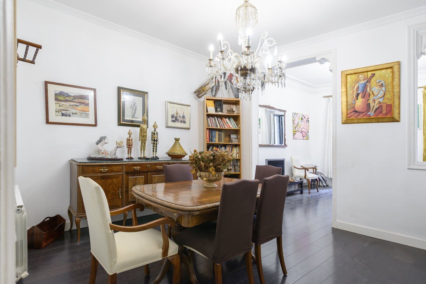 Une salle à manger avec une table en bois, des chaises, un lustre et une bibliothèque remplie de livres.